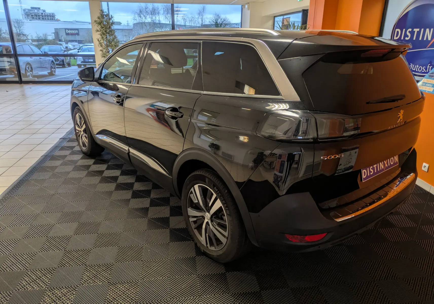 Vue 3/4 arrière droite d’un Peugeot 5008 noir 2024 en showroom avec vitres arrière surteintées et jantes aluminium 18 pouces.