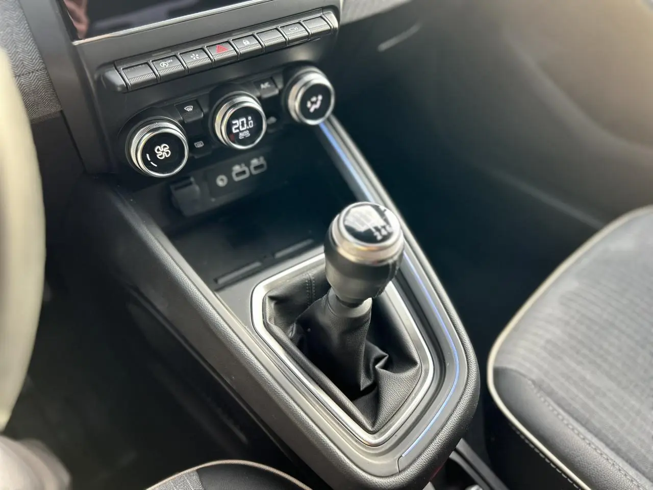Gros plan sur la console centrale d’une Renault Clio 2025, boîte manuelle avec commandes de climatisation et sièges gris.
