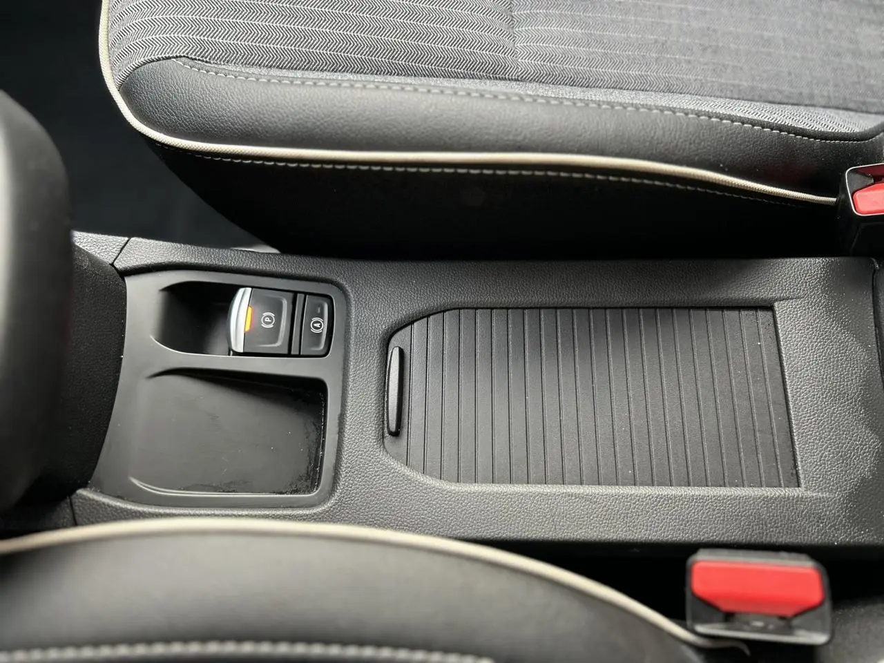 Vue rapprochée de la console centrale noire avec frein de parking électrique et accoudoir coulissant de la Renault Clio Rouge Désir.
