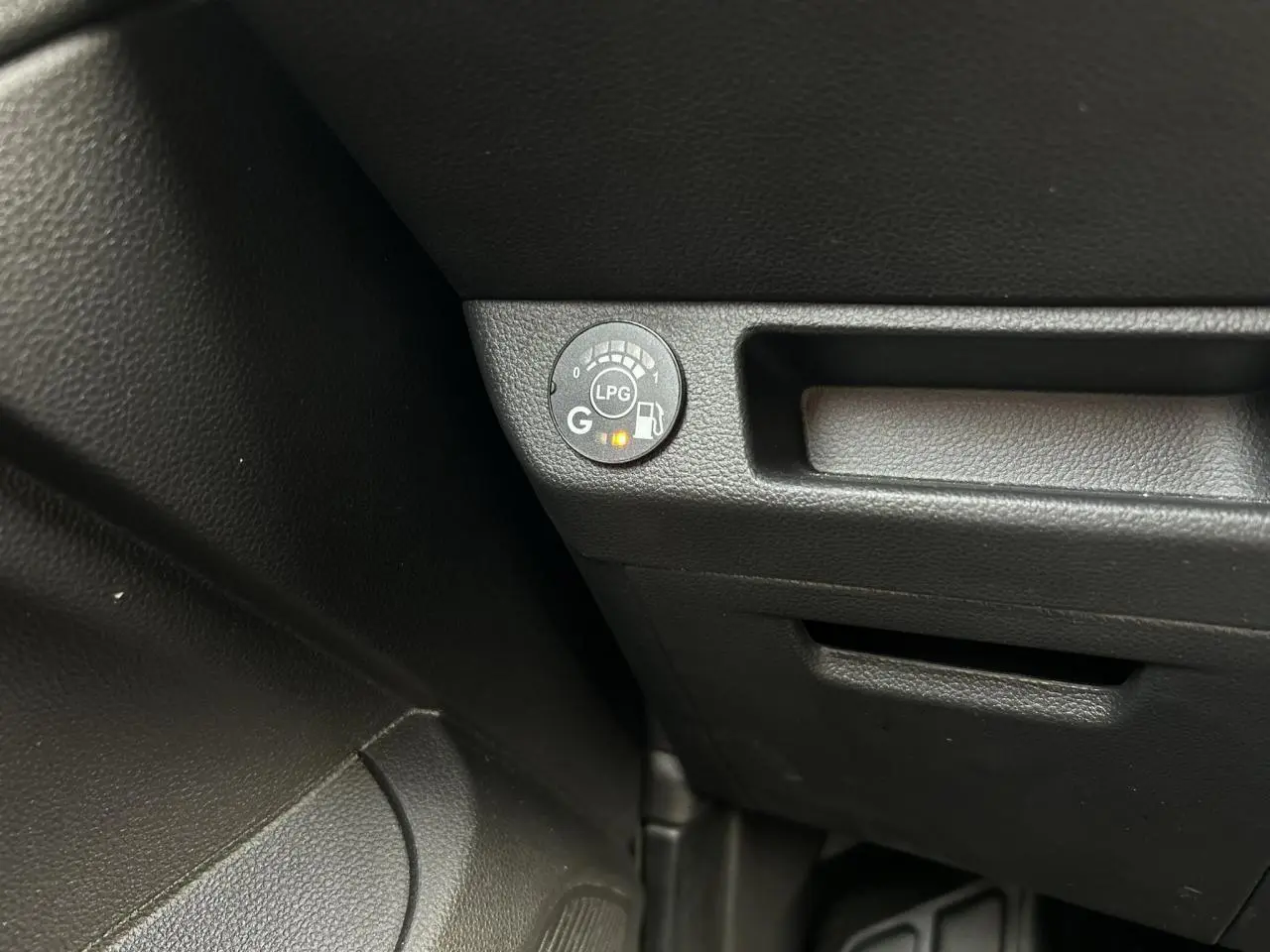 Gros plan sur le bouton de contrôle GPL noir dans l’habitacle de la Renault Clio Rouge Désir.