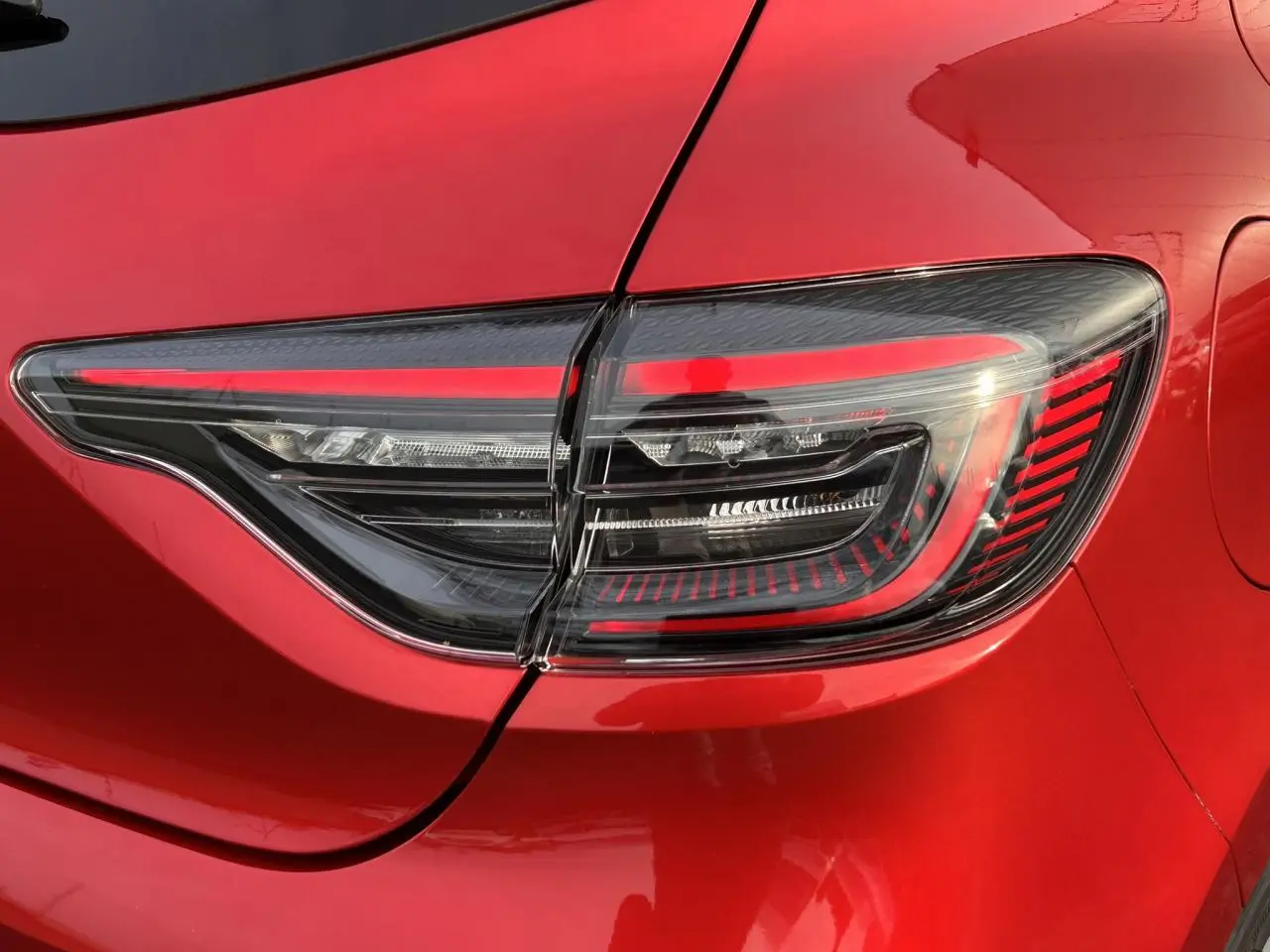 Gros plan sur le feu arrière droit de la Renault Clio 2025 Rouge Désir avec signature lumineuse LED en forme de C.