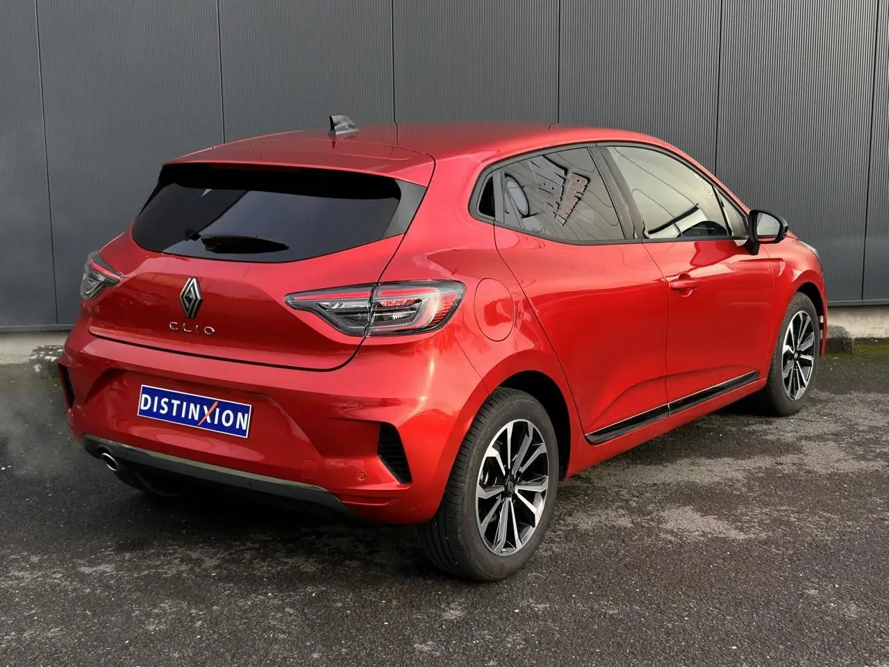 Vue 3/4 arrière droite d'une Renault Clio Rouge Désir avec jantes alliage et vitres surteintées.