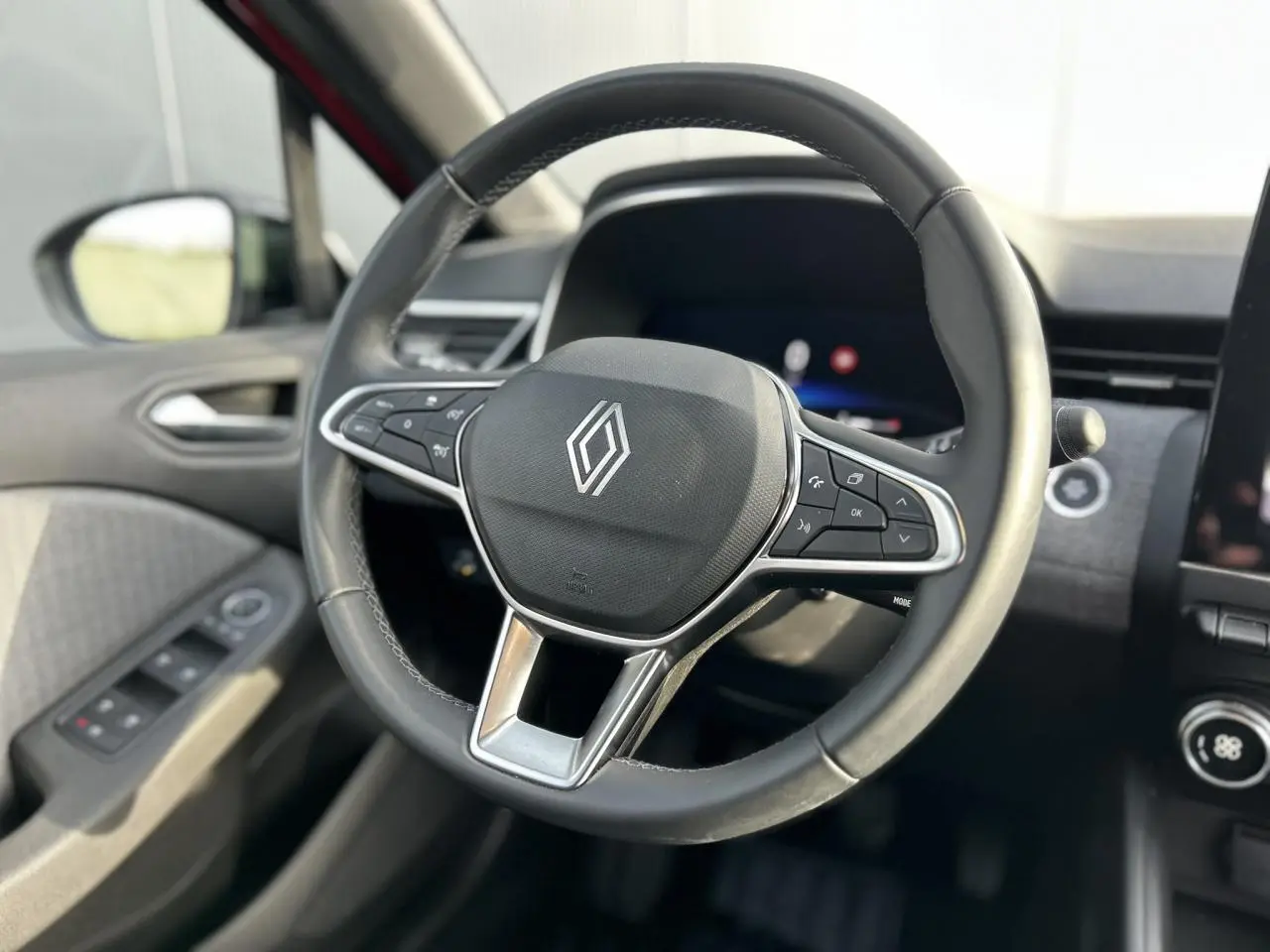 Gros plan sur le volant multifonction noir de la Renault Clio 2025, avec commandes intégrées et tableau de bord flou en arrière-plan.