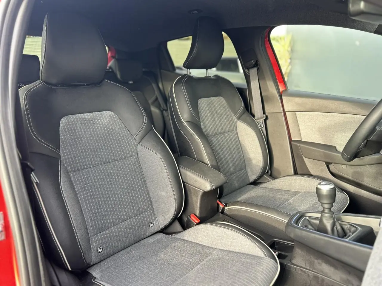 Vue intérieure côté avant gauche montrant les sièges tissu et cuir gris avec surpiqûres blanches d'une Renault Clio Rouge Désir.