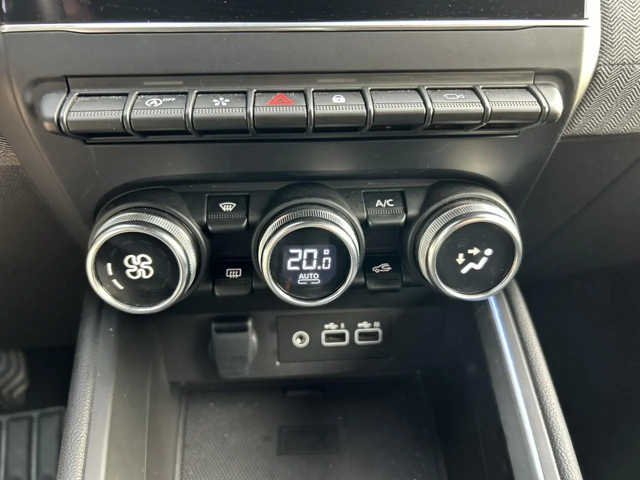 Gros plan sur la console centrale de la Renault Clio 2025, boutons de climatisation et ports USB visibles.