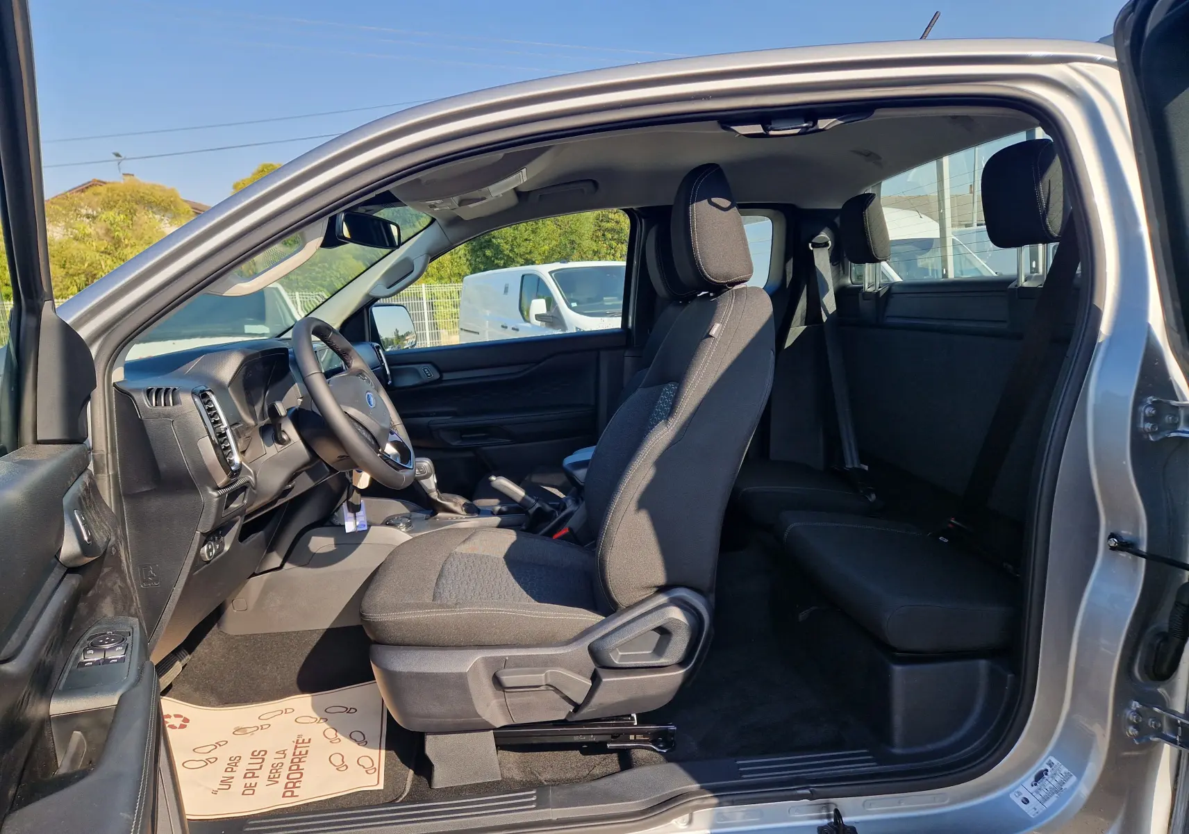Vue intérieure côté gauche du Ford Ranger Super Cabine gris Iconic 2026, montrant les sièges avant et arrière ainsi que le tableau de bord.