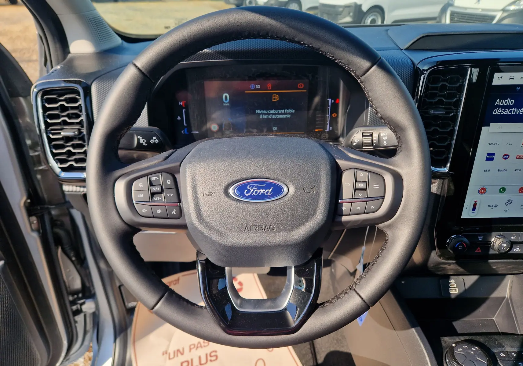 Vue rapprochée du volant noir du Ford Ranger Super Cabine 2026 gris, avec commandes intégrées et tableau de bord digital.