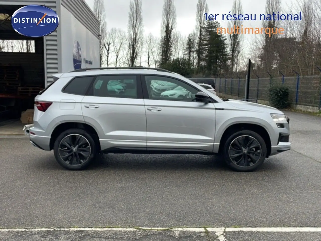 Vue de profil côté gauche d’un Skoda Karoq gris argent métallisé 2025 avec jantes noires et toit panoramique.