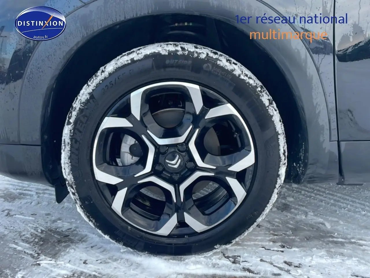 Gros plan sur la roue avant droite noire avec jante alu bicolore du Citroën C5 Aircross noir sous la neige.