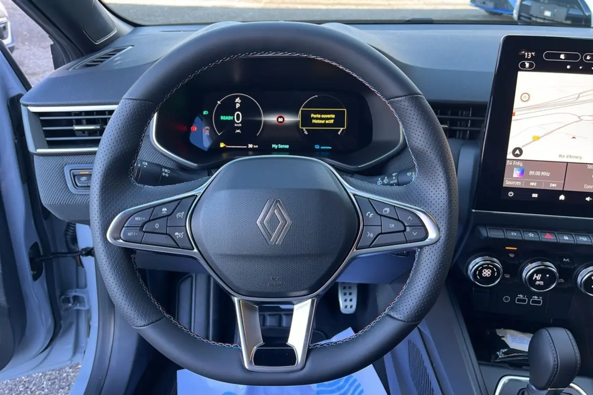 Vue rapprochée du volant cuir multifonctions de la Renault Clio V E-Tech 145 Esprit Alpine avec tableau de bord numérique et écran tactile.