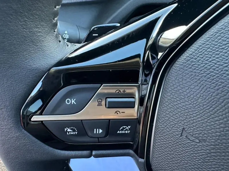 Gros plan sur les commandes gauche du volant noir du Peugeot 308 SW 2024, boutons multifonctions avec finition brillante.