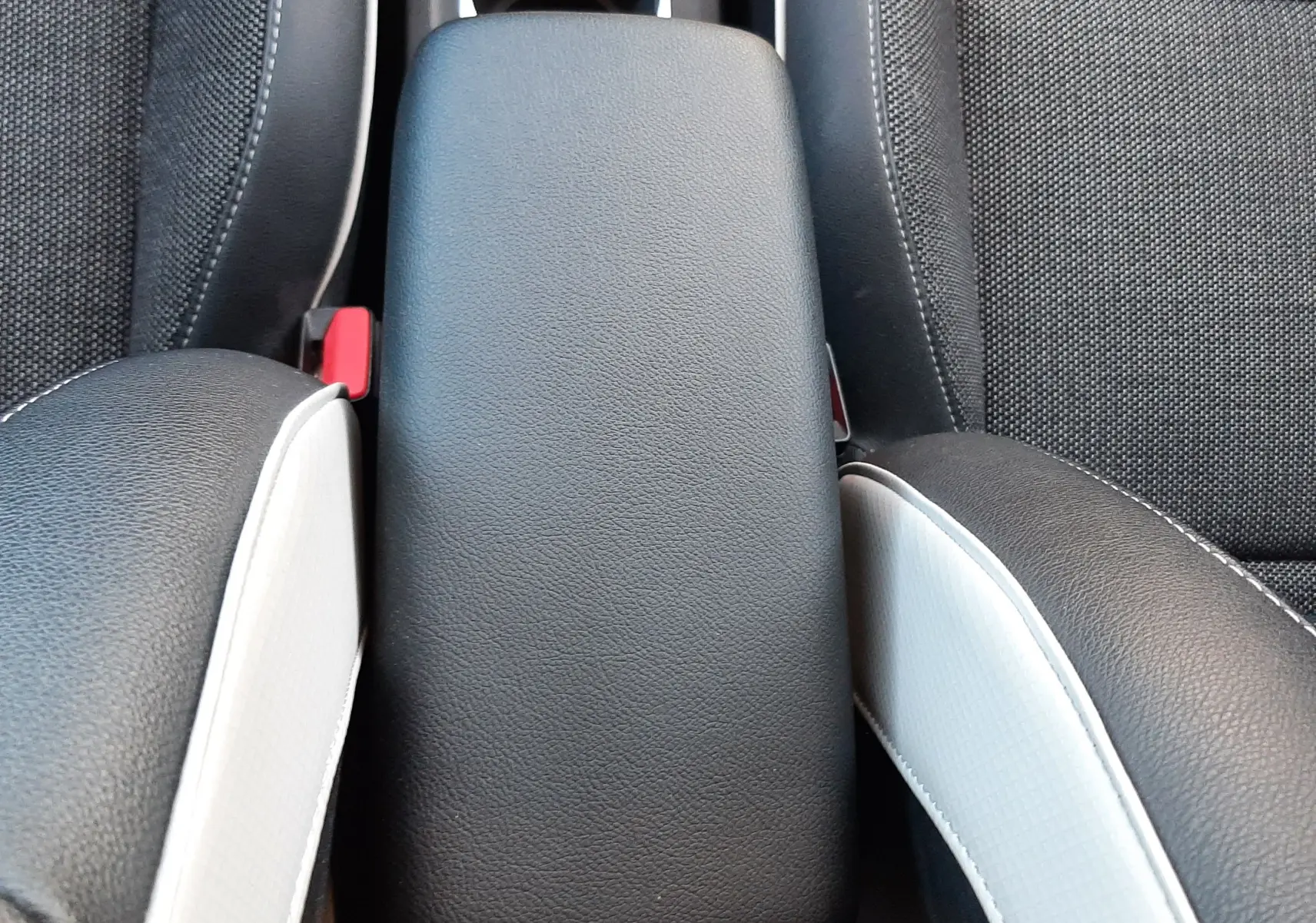 Vue plongeante sur l'accoudoir central noir entre les sièges avant en tissu noir et blanc du Renault Captur E-Tech 2022.