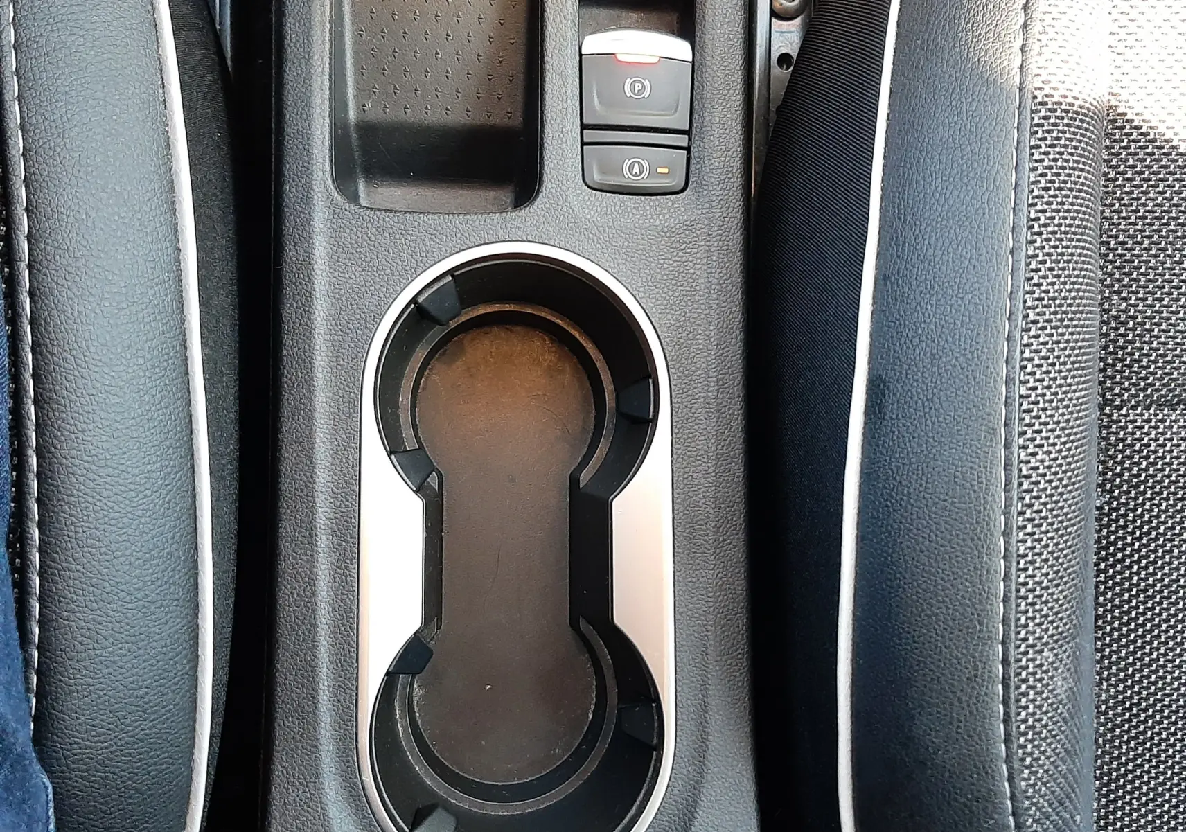 Vue plongeante sur la console centrale noire du Renault Captur E-Tech 145ch Intens, avec porte-gobelets et bouton de frein à main électrique.