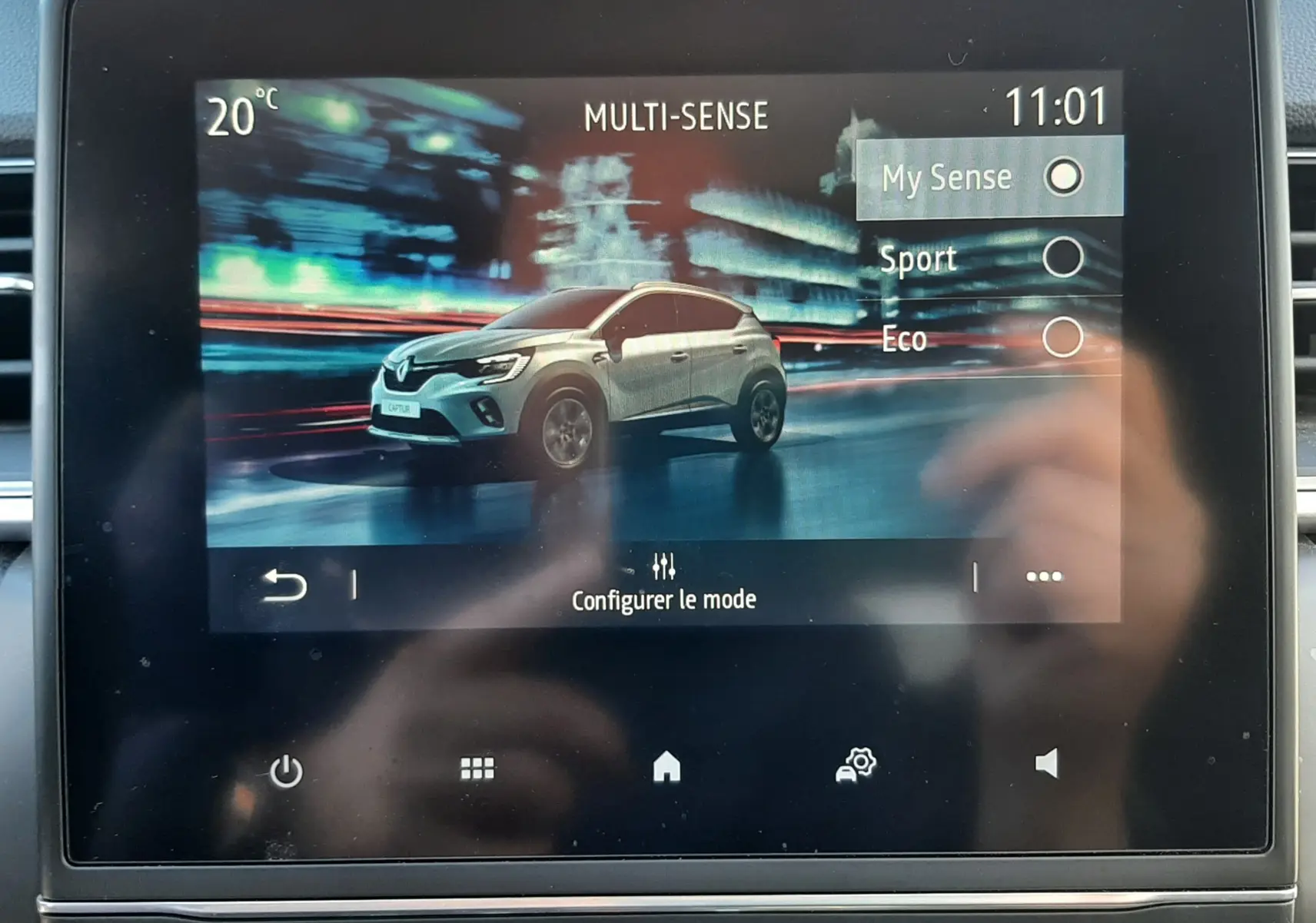 Écran tactile affichant un Renault Captur E-Tech blanc nacré à 3/4 avant dans un décor urbain nocturne flouté.