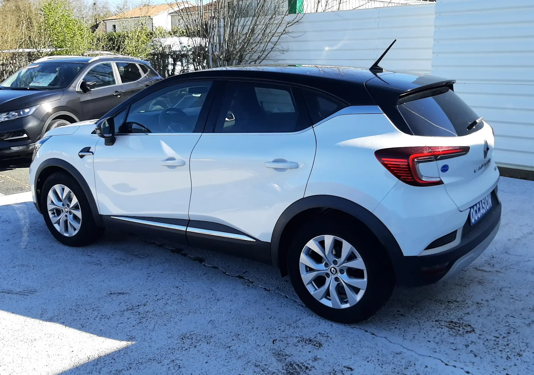 Renault Captur E-Tech 145ch Intens blanc nacré avec toit noir, vue 3/4 arrière côté droit sur parking extérieur.