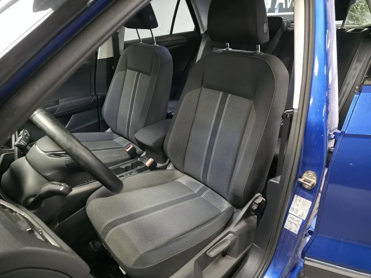 Vue intérieure côté conducteur du Volkswagen T-Roc bleu foncé, mettant en valeur les sièges avant en tissu gris avec accoudoir central.