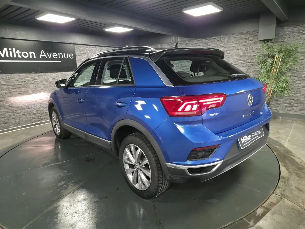 Volkswagen T-Roc bleu foncé en 3/4 arrière droit, avec jantes alliage argent et toit noir contrasté.