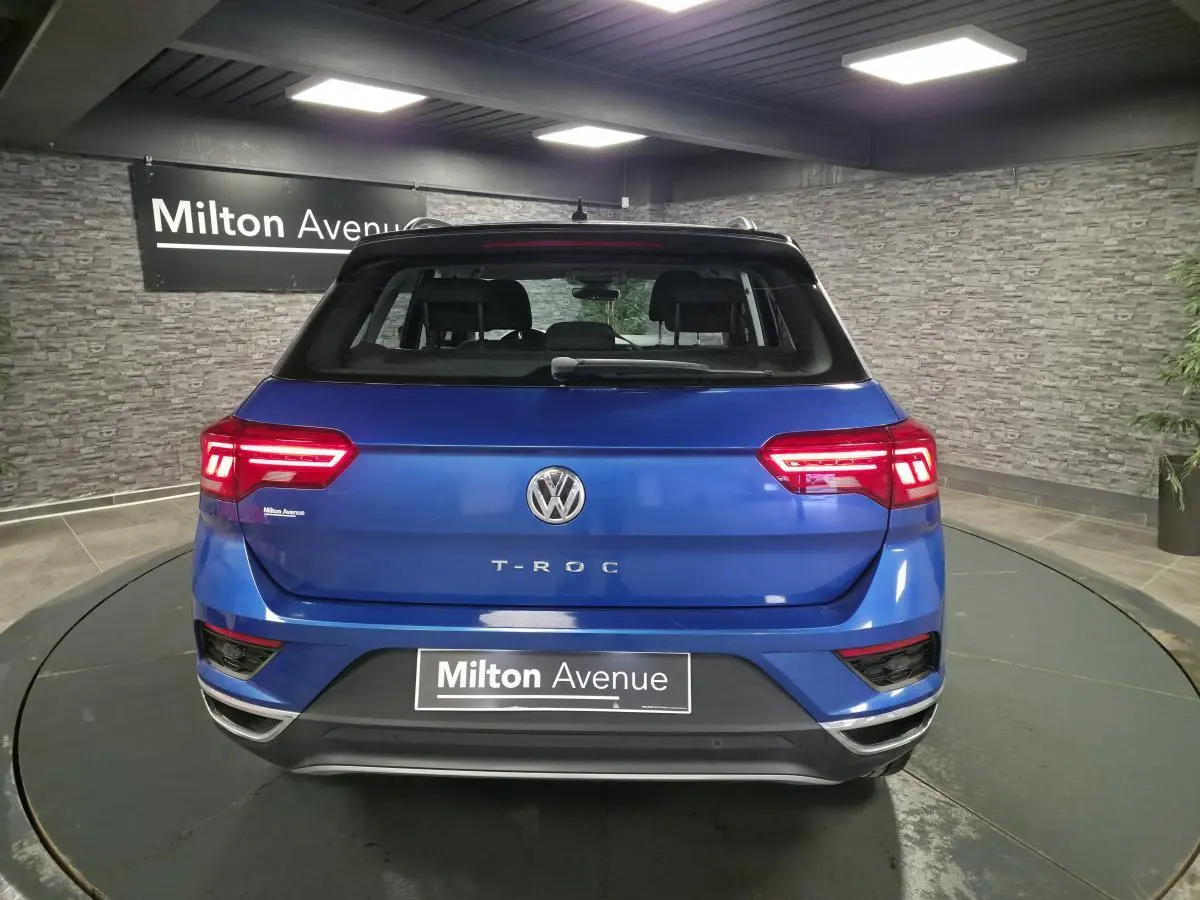 Vue arrière d'un Volkswagen T-Roc bleu foncé avec feux LED allumés dans un showroom intérieur.