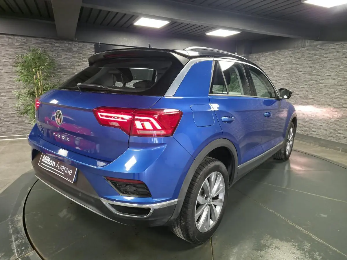 Vue 3/4 arrière droite d'un Volkswagen T-Roc bleu foncé avec toit noir et jantes alliage argentées en intérieur showroom.