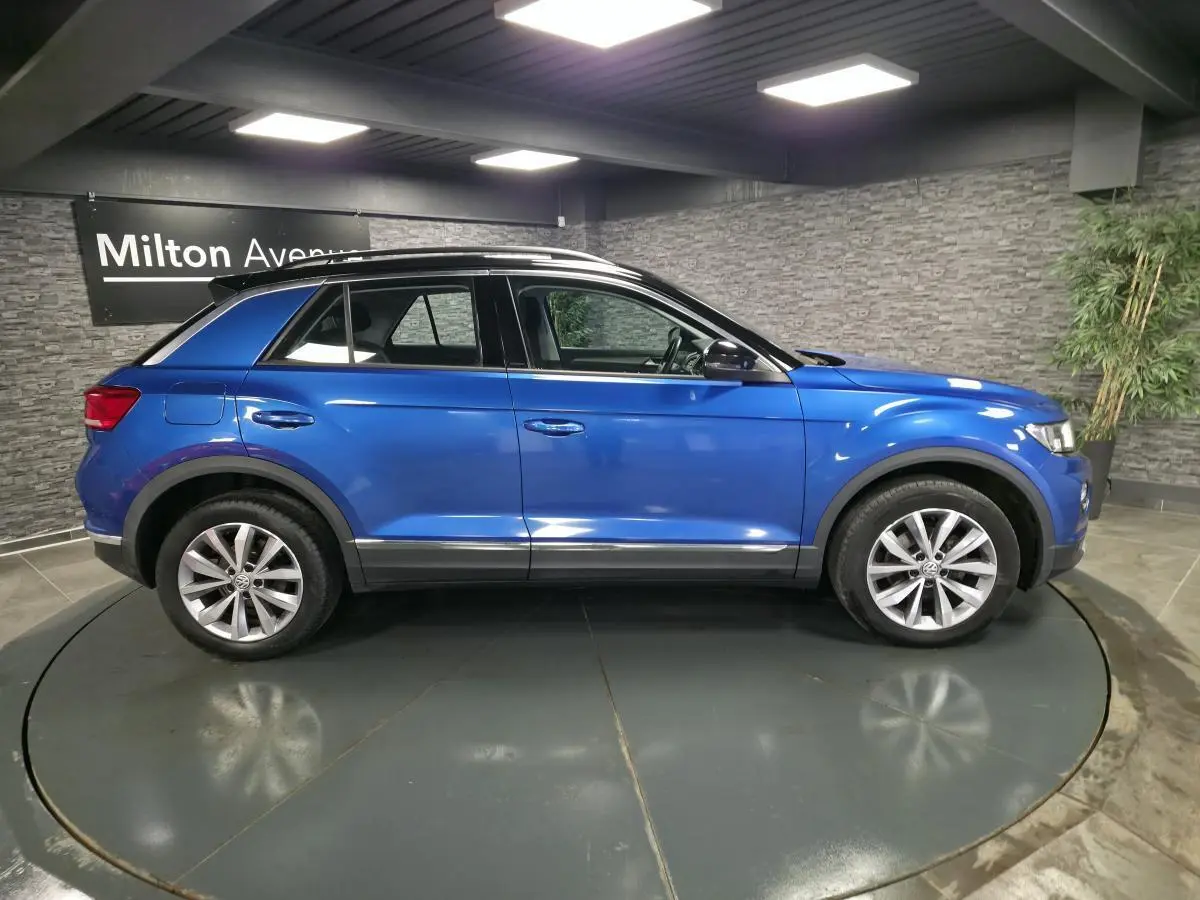 Vue de profil côté gauche d'un Volkswagen T-Roc bleu foncé avec jantes alliage 17 pouces dans un showroom.
