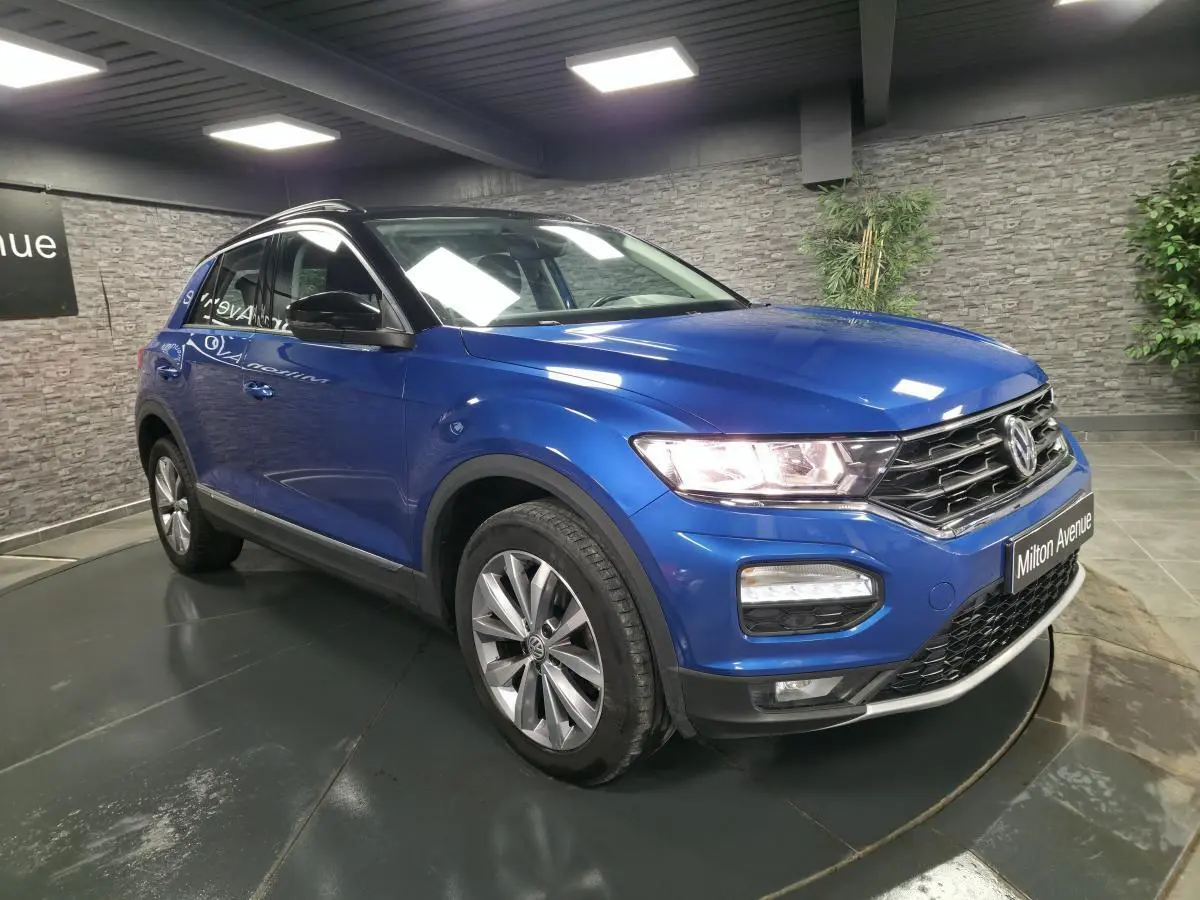 Volkswagen T-Roc bleu foncé en 3/4 avant droit, avec jantes alliage et calandre chromée visible.
