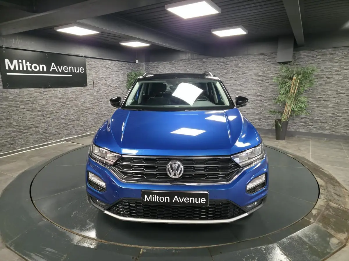 Vue avant d'un Volkswagen T-Roc bleu foncé avec calandre noire et toit noir dans un showroom.