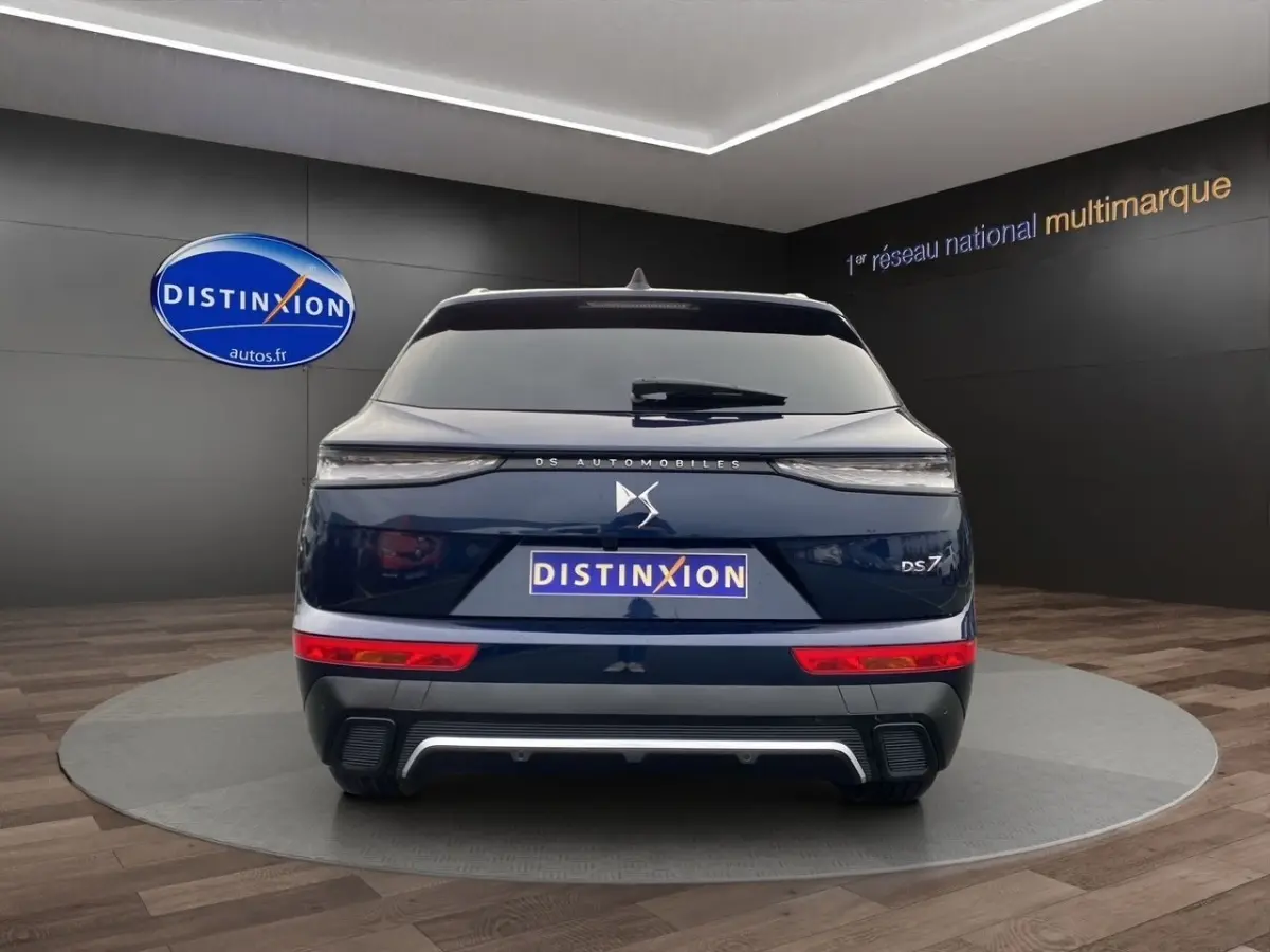 Vue arrière d'un DS7 Crossback bleu 2024 avec feux LED fins et logo DS centré sur un fond showroom.