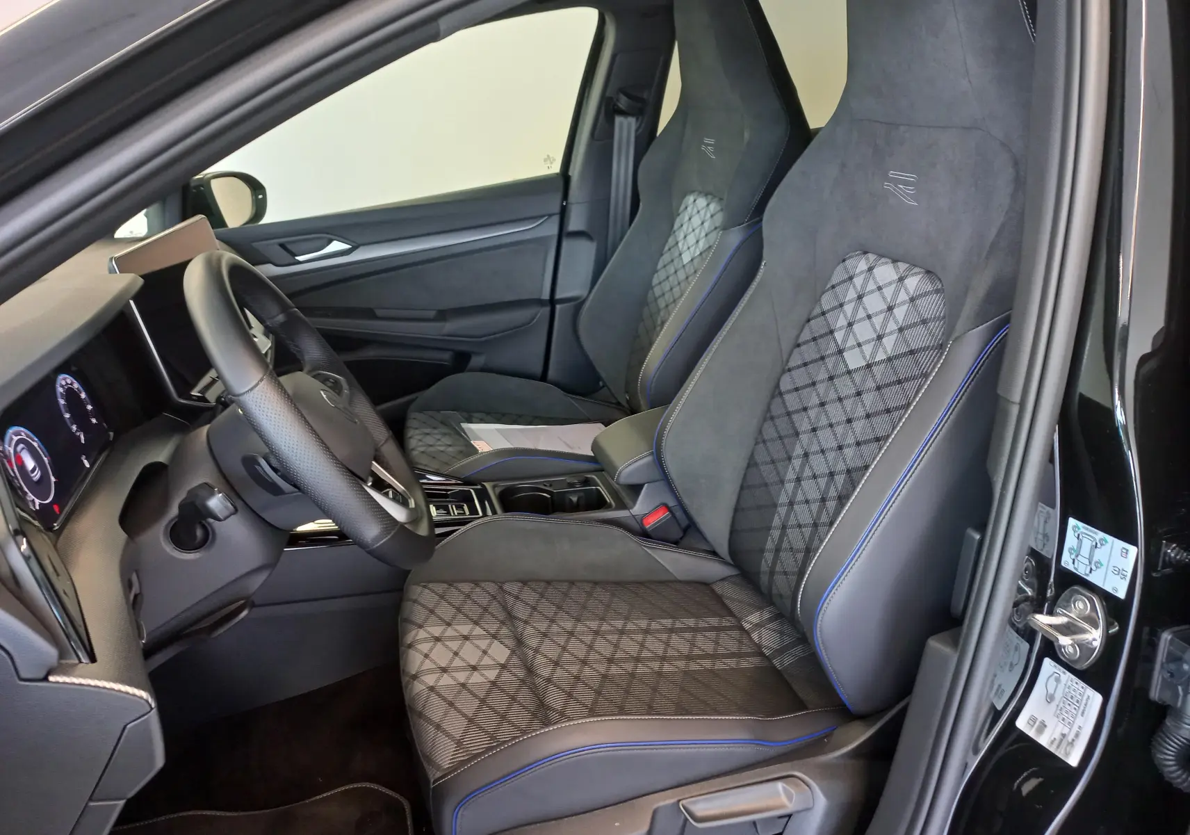 Vue intérieure côté conducteur de la Volkswagen Golf 1.5 eTSI R-Line 2025 avec sièges sport en tissu et alcantara noir.