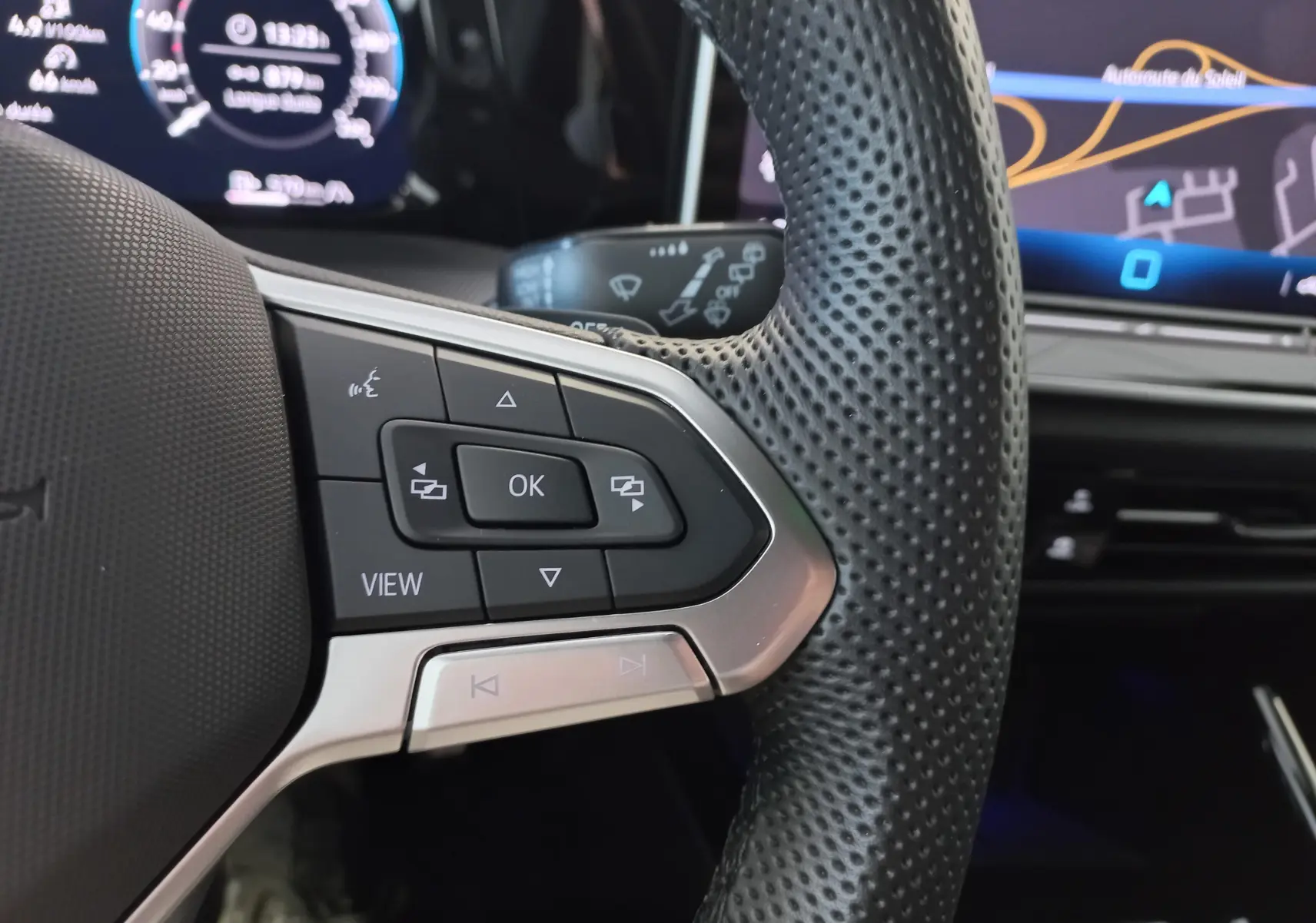 Gros plan sur les commandes gauche du volant perforé d'une Volkswagen Golf 1.5 eTSI 2025, tableau de bord numérique en arrière-plan.