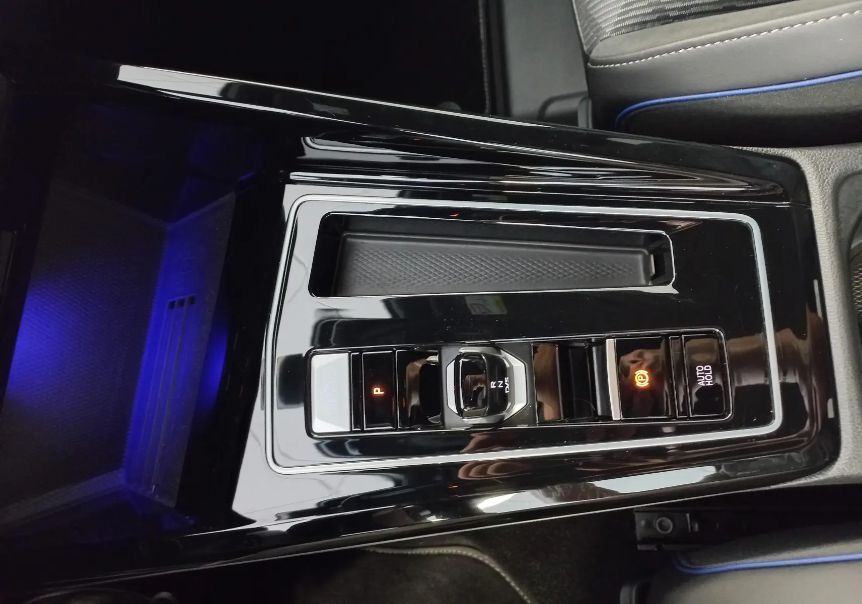 Vue rapprochée de la console centrale noire brillante de la Volkswagen Golf 1.5 eTSI avec sélecteur de boîte auto et éclairage bleu.