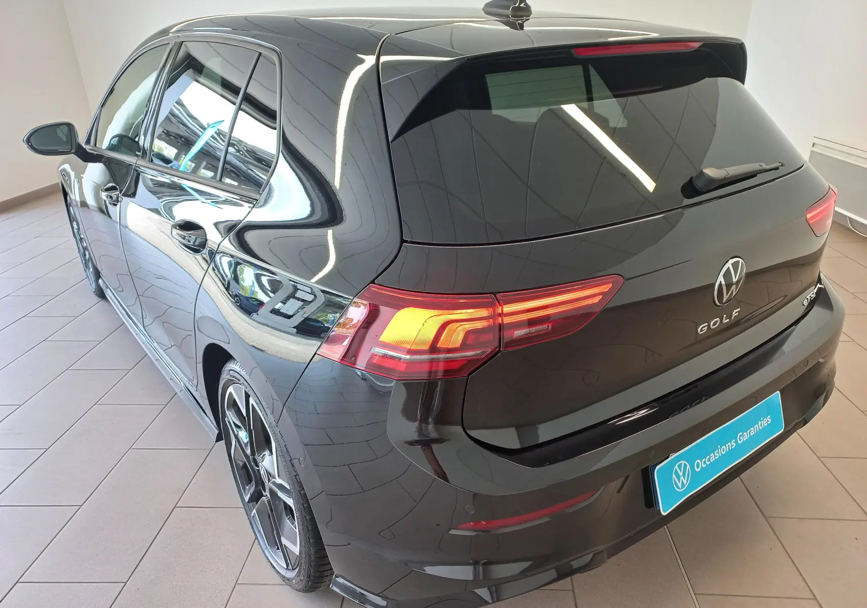 Vue 3/4 arrière droite d'une Volkswagen Golf 1.5 eTSI R-Line noire Ébène avec feux LED et jantes alliage sport.