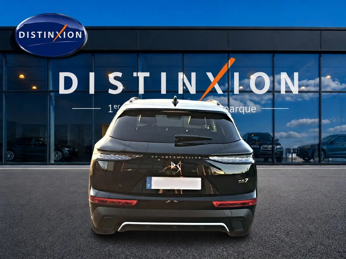 Vue arrière d'un DS7 noir 2026 garé devant une vitrine avec logo Distinxion, feux arrière LED visibles.