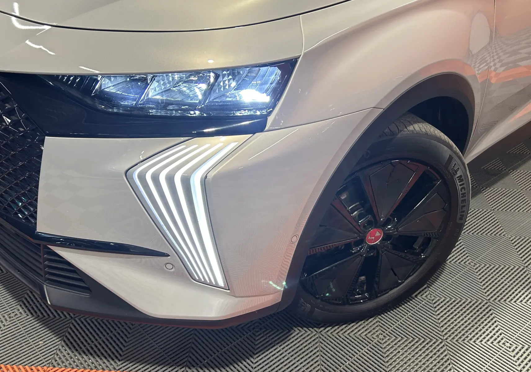 Gros plan sur l'avant droit du DS7 Cristal Pearl 2024, mettant en valeur les feux LED distinctifs et la jante noire.