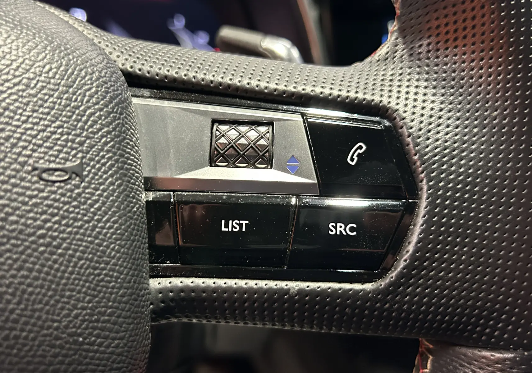 Gros plan sur les commandes noires du volant perforé côté gauche du DS7 BlueHDi 130 2024, boutons LIST et SRC visibles.