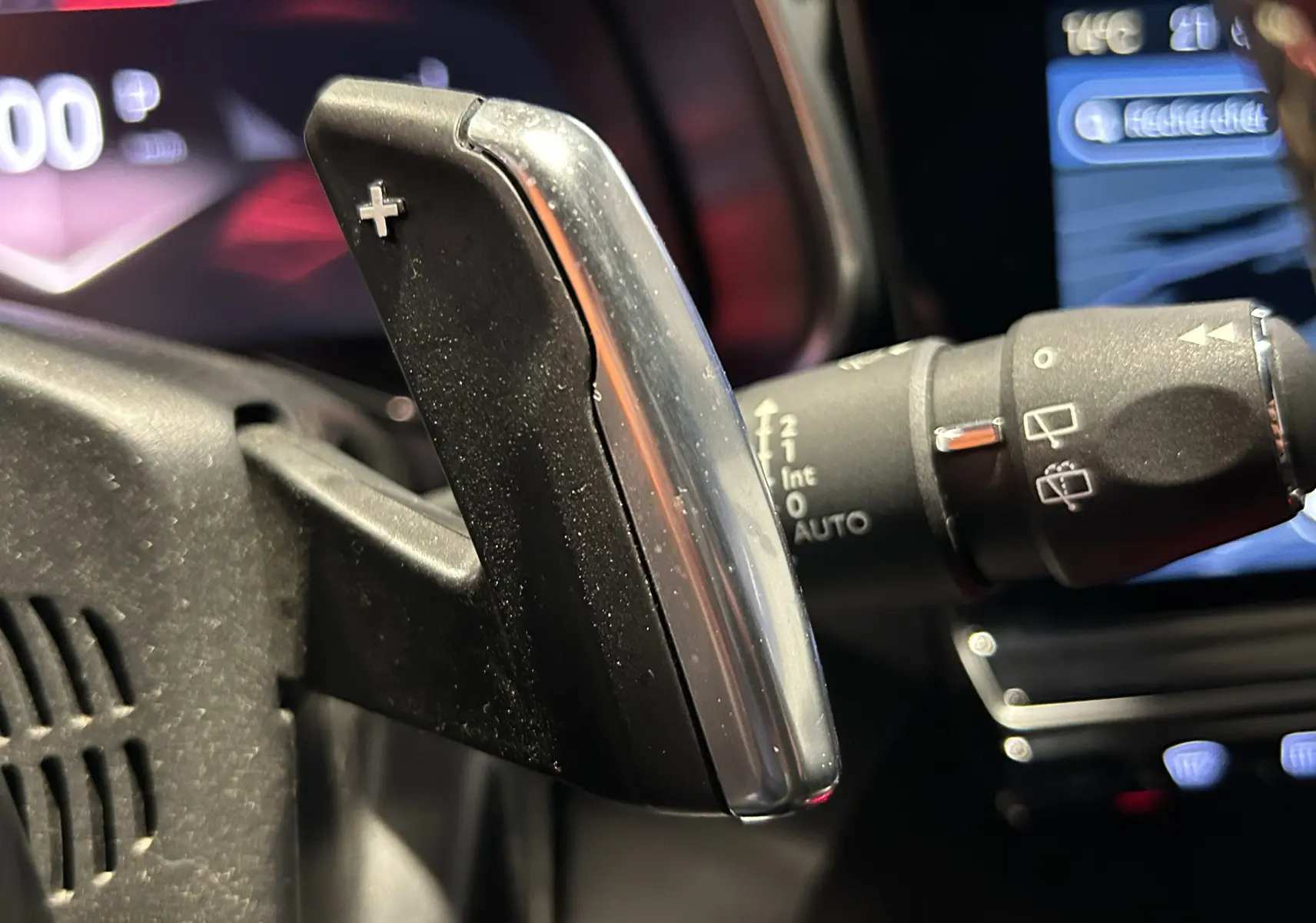 Gros plan sur la palette de changement de vitesse + au volant du DS7 2024, intérieur noir avec commandes visibles en arrière-plan.