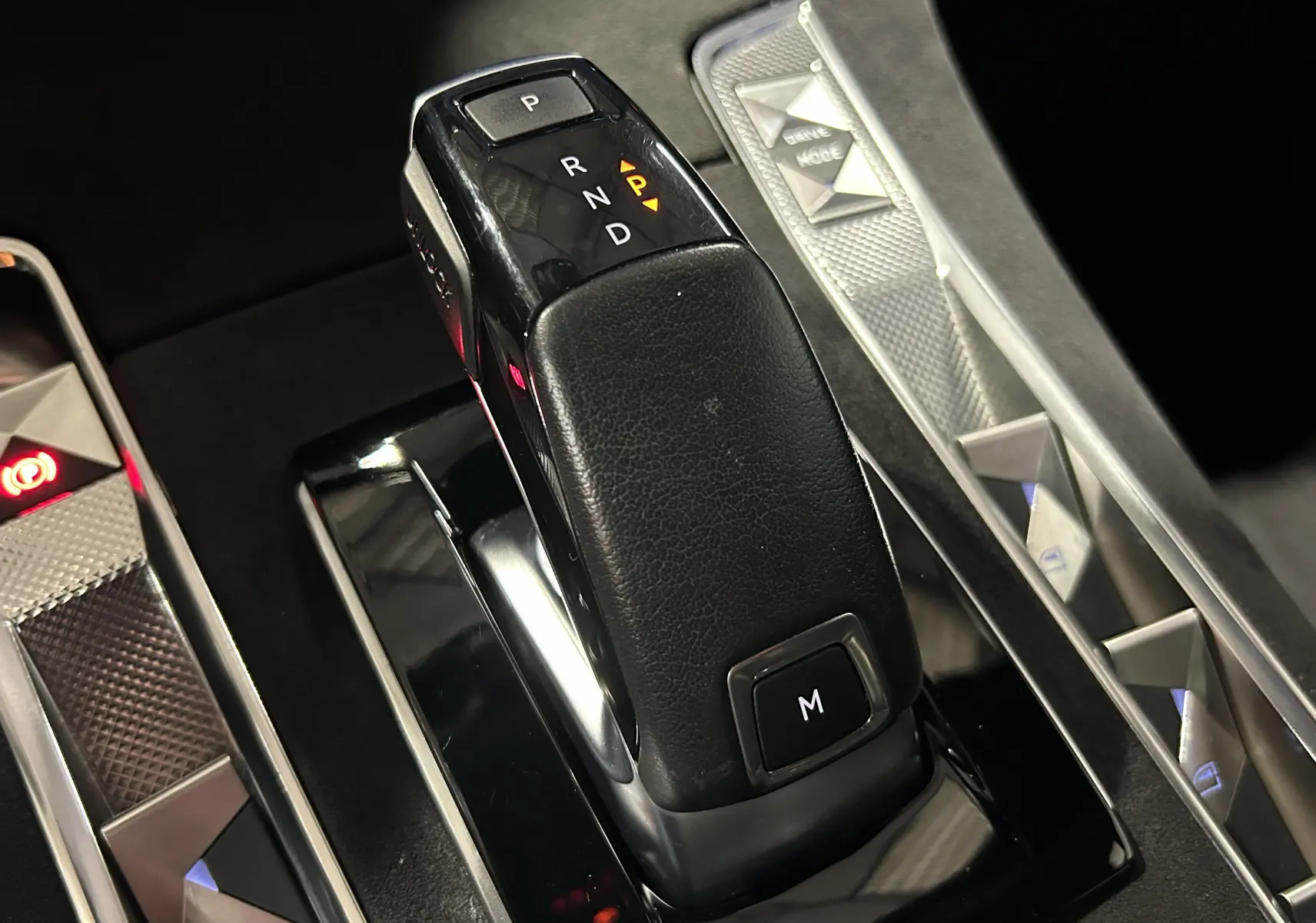 Le levier de vitesses automatique noir en cuir du DS7 2024, avec boutons de commande et éclairage ambiant visible.