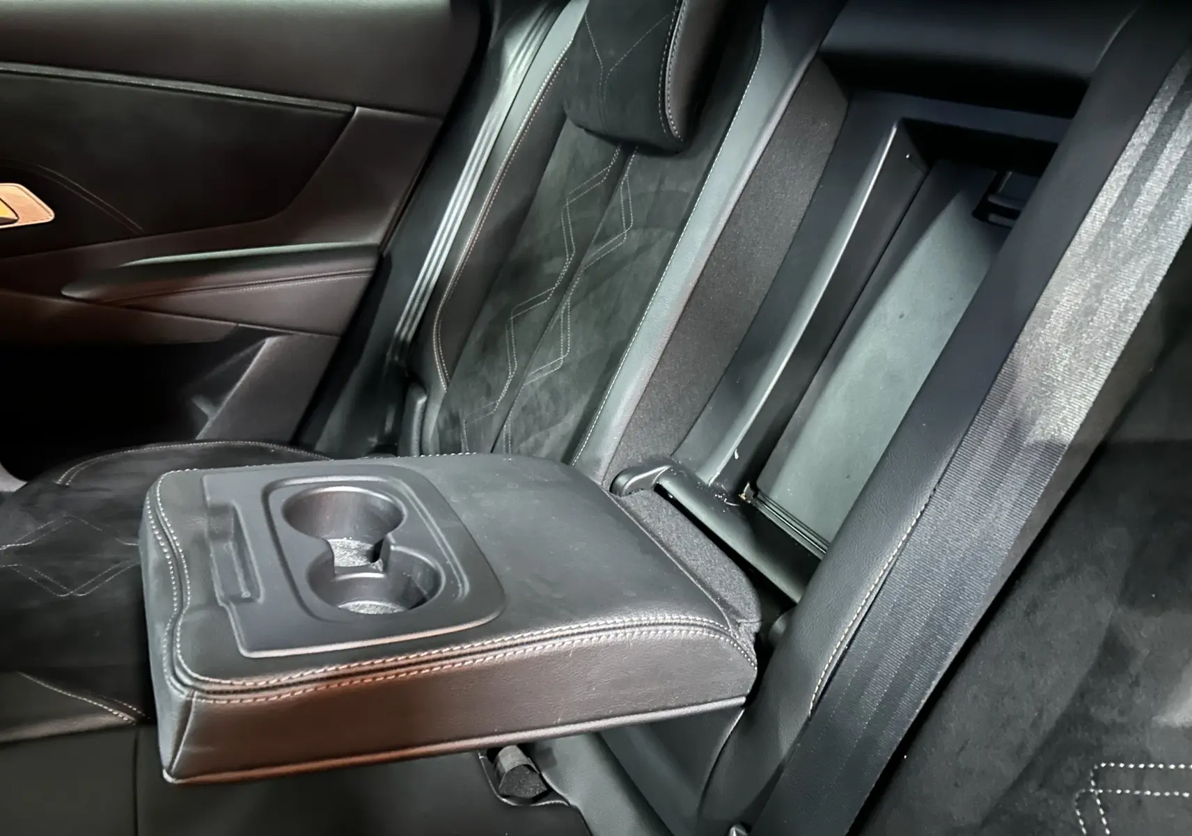Vue rapprochée de l'accoudoir central arrière en cuir noir avec porte-gobelets, sièges arrière en alcantara du DS7 2024.