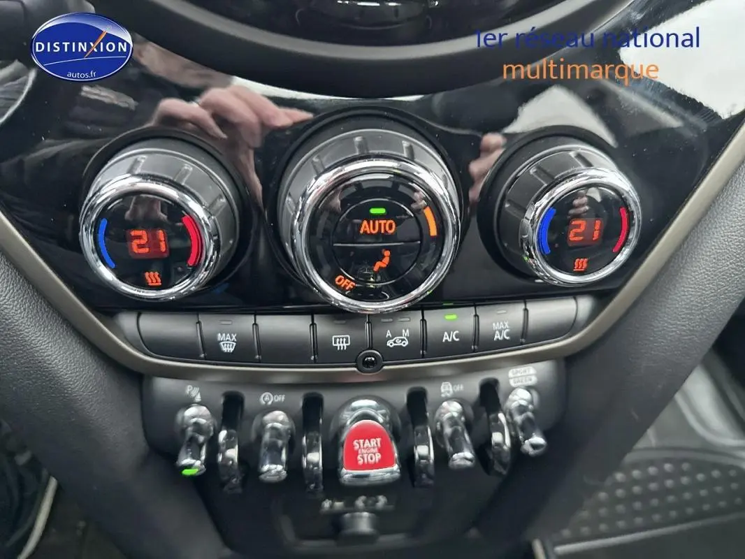 Gros plan sur la console centrale du MINI Countryman noir, montrant les commandes de climatisation automatique et le bouton start/stop rouge.