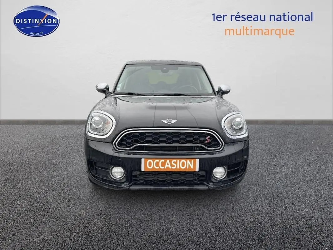 Vue frontale d'une MINI Countryman noire avec calandre hexagonale et feux avant allumés sur fond neutre.