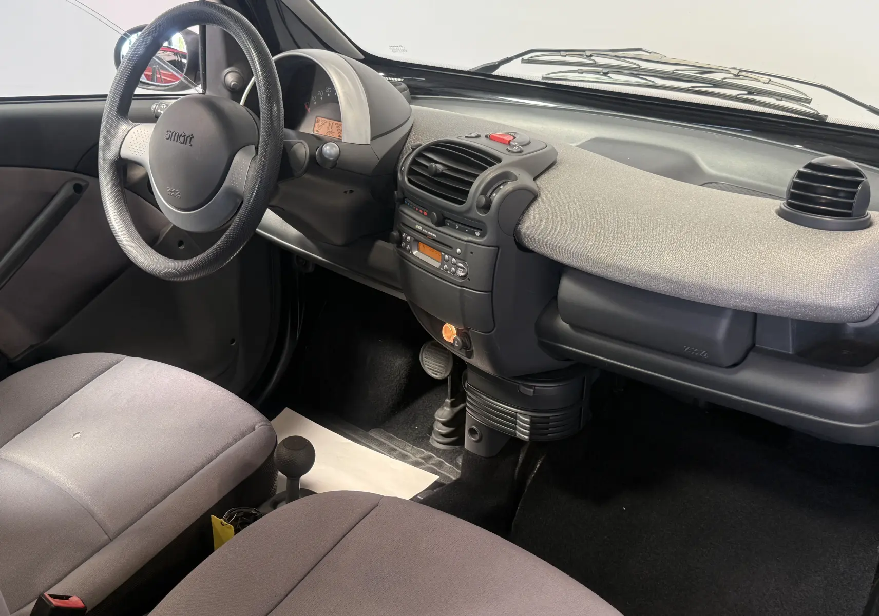 Intérieur de la Smart Fortwo Coupé 2004 vu côté conducteur, tableau de bord gris clair et sièges tissu gris.