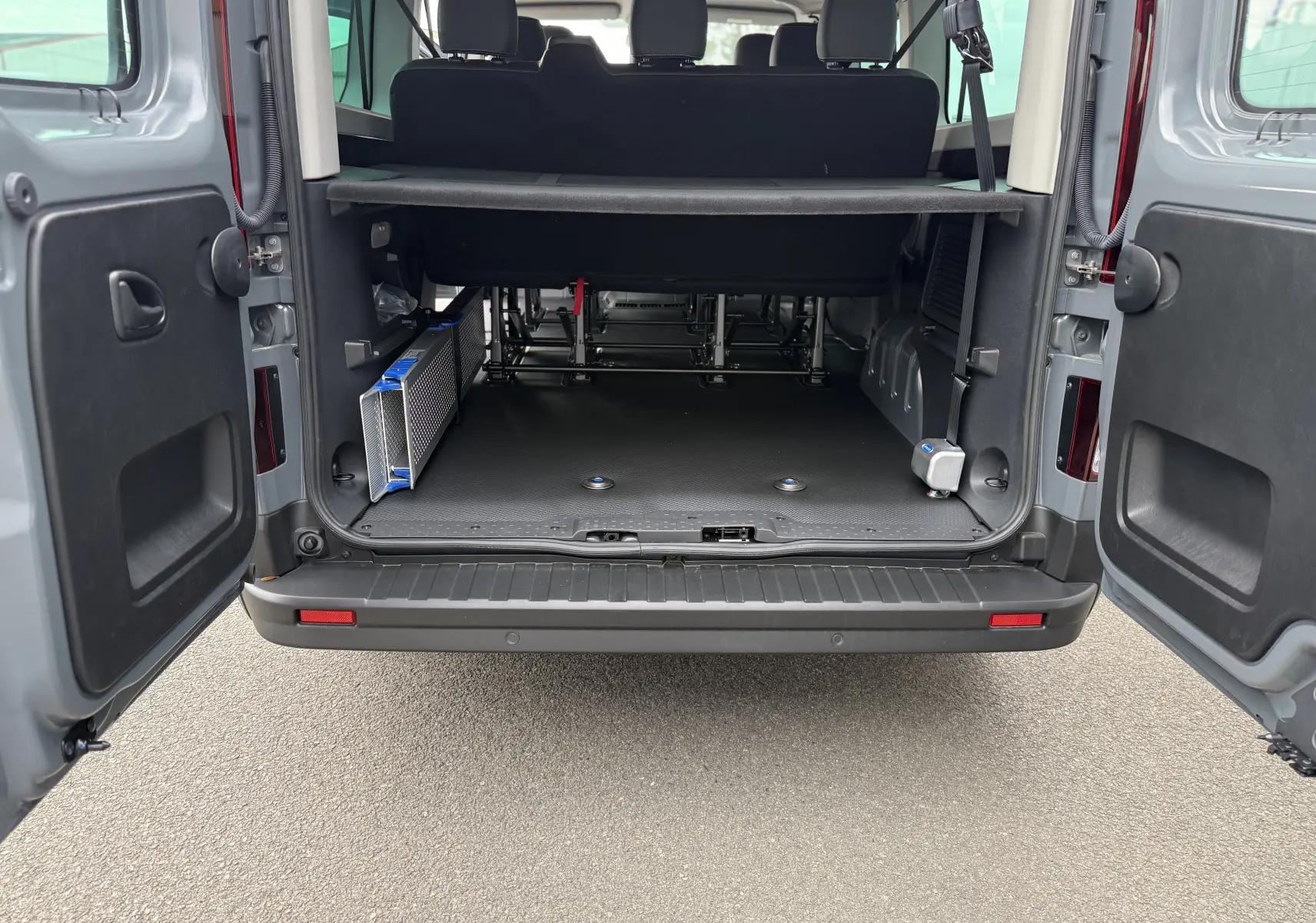 Vue arrière du Renault Trafic Combi gris urbain 2025 avec portes ouvertes montrant l'espace de chargement et l'adaptation pour fauteuil roulant.