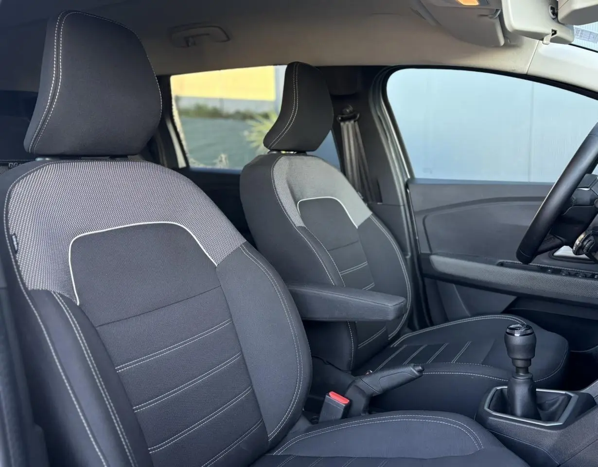 Vue intérieure côté conducteur du Dacia Jogger gris Schiste 2025, avec sièges tissu noirs et levier de vitesses manuel.