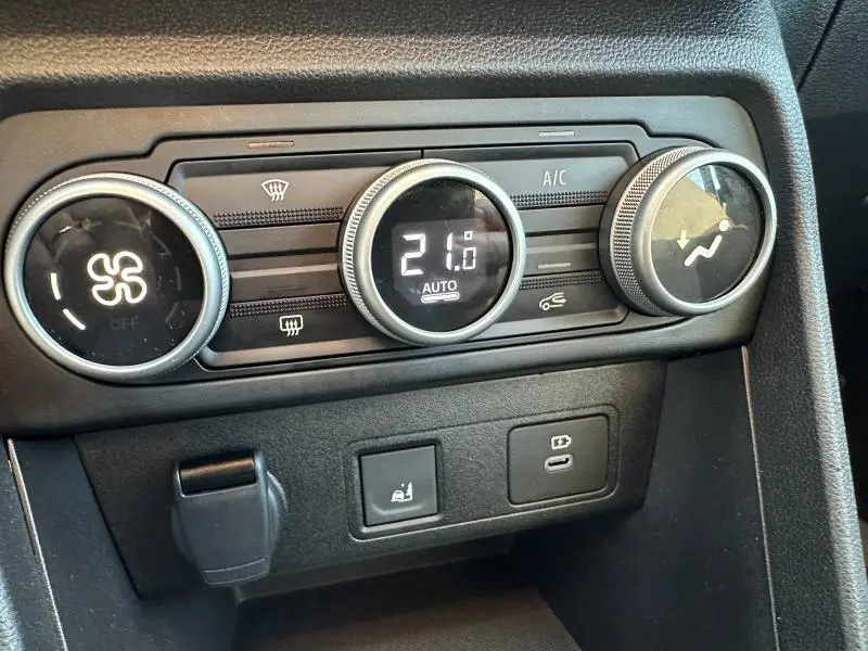 Gros plan sur les commandes de climatisation digitale et les boutons USB et siège chauffant du tableau de bord d'une Dacia Sandero blanche.