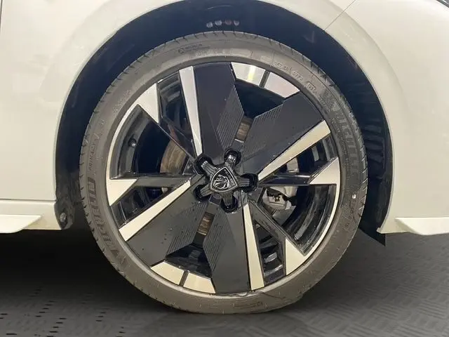 Gros plan sur la roue avant droite d'une Peugeot 308 Hybrid 145 e-DCS6 GT blanche avec jante alliage noire et argent.