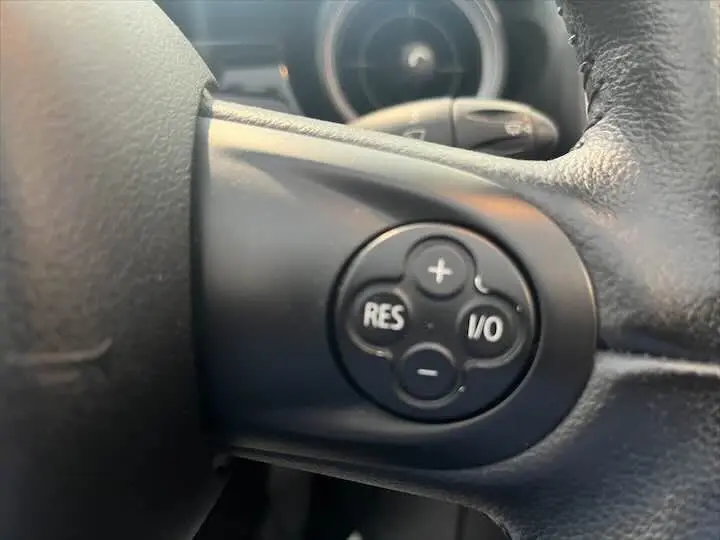 Gros plan sur les commandes de régulateur de vitesse sur le volant d'une MINI Cooper Cabriolet noire de 2012.