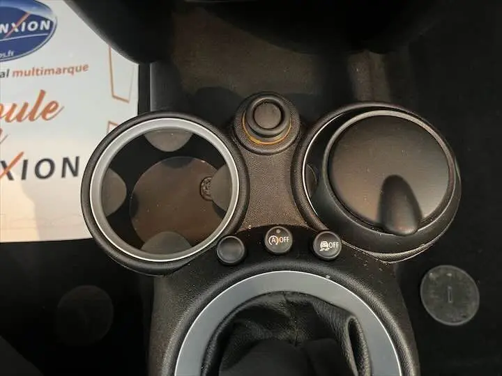 Gros plan sur la console centrale d'une MINI Cooper Cabriolet noire de 2012, montrant les commandes et porte-gobelets.