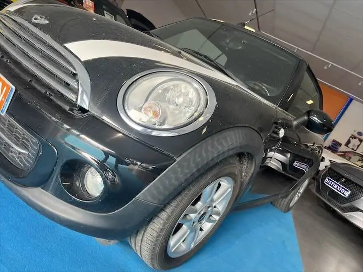 Vue en gros plan 3/4 avant gauche d'une MINI Cooper Cabriolet noire avec bandes blanches sur le capot, en showroom.
