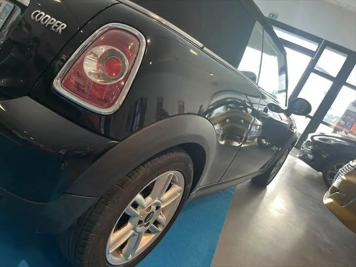 Vue 3/4 arrière gauche d'une MINI Cooper cabriolet noire, mettant en valeur le feu arrière et la jante alu.
