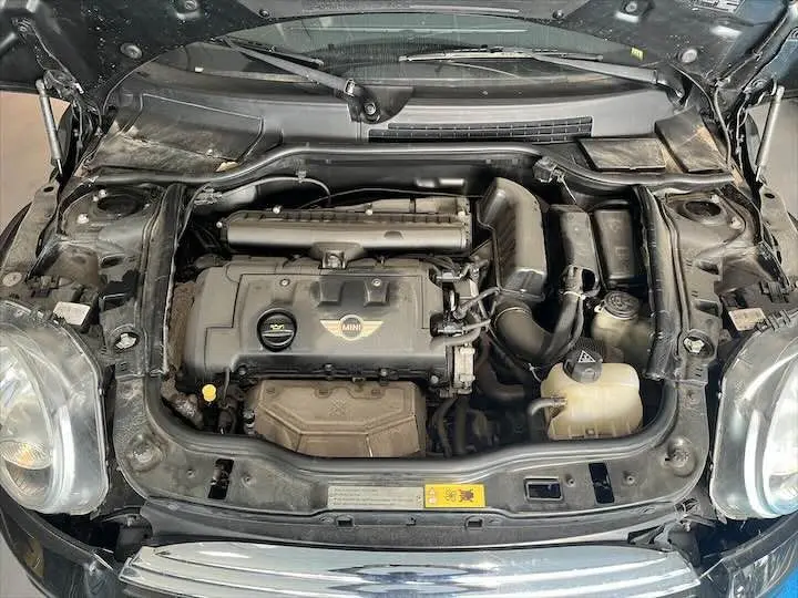 Vue plongeante sur le moteur noir d'une MINI Cooper Cabriolet 2012 avec capot ouvert et logo MINI visible.