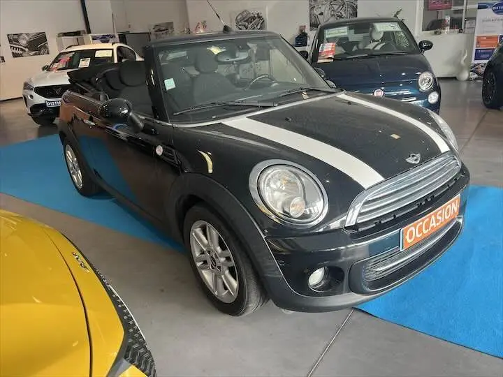 Vue 3/4 avant droite d'une MINI Cooper Cabriolet noire avec bandes blanches et toit ouvert en concession.